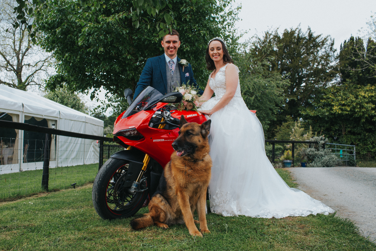 bride and groom on a motorbike with their german shepherd