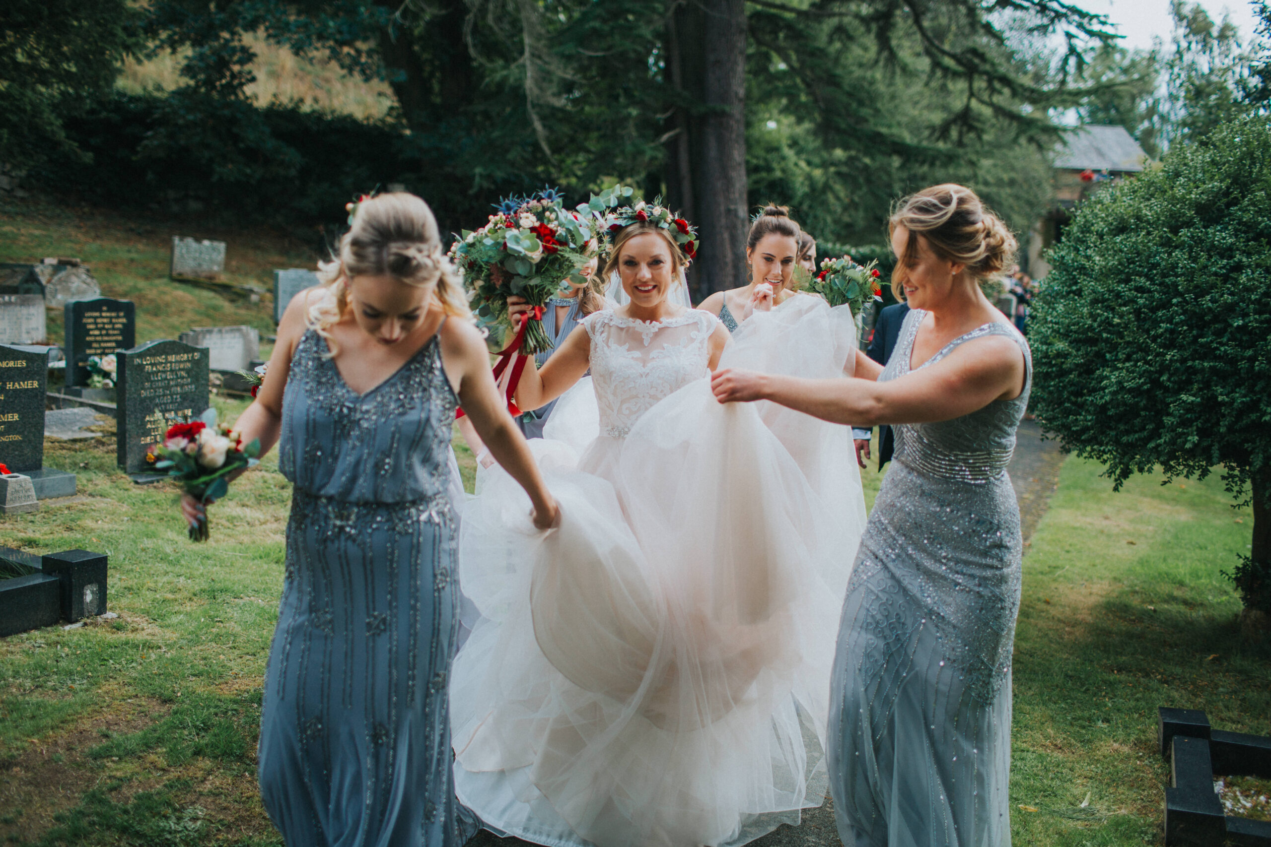 bride walking up church path with bridesmaids helping with her dress