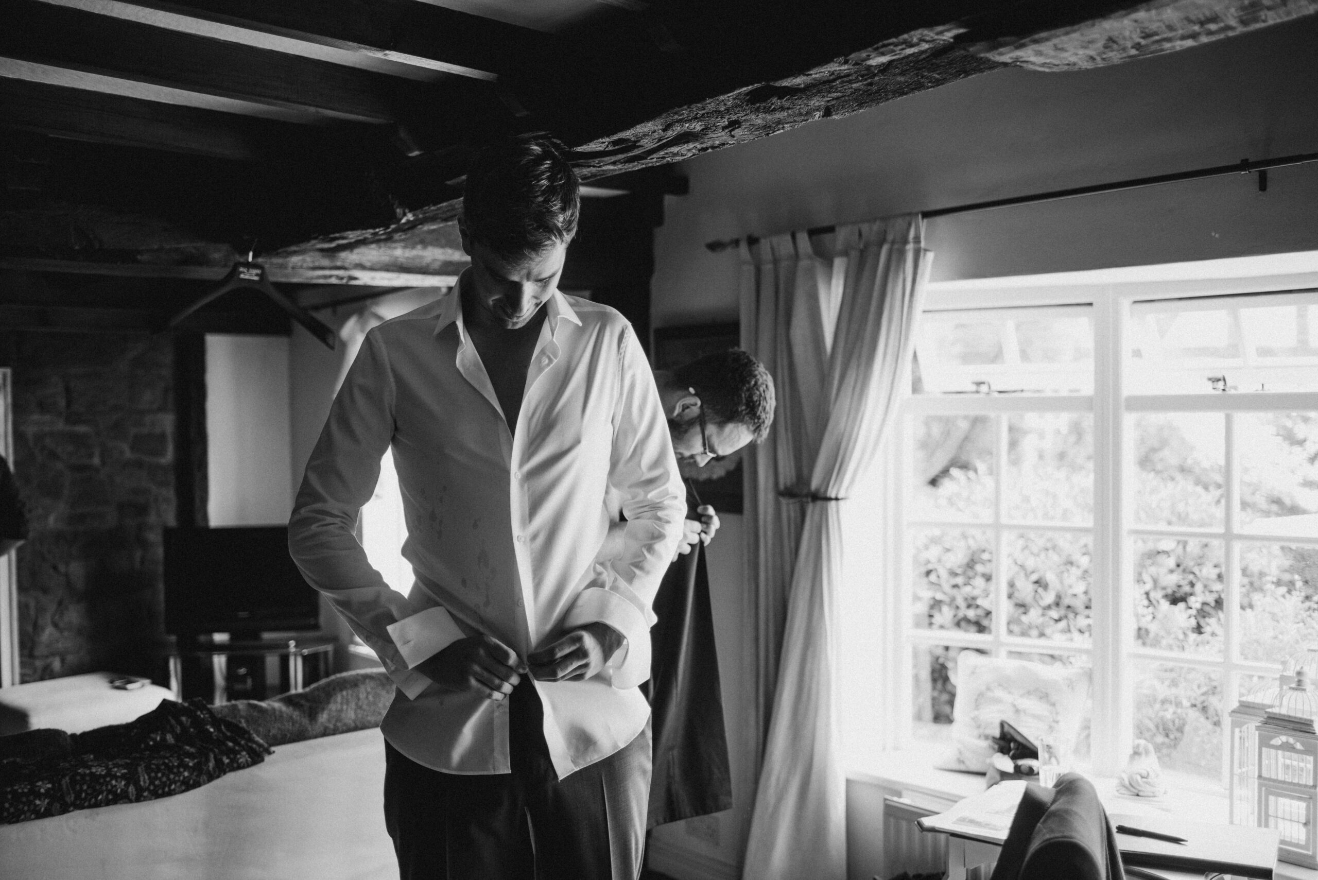 black and white photo of groom doing his shirt up