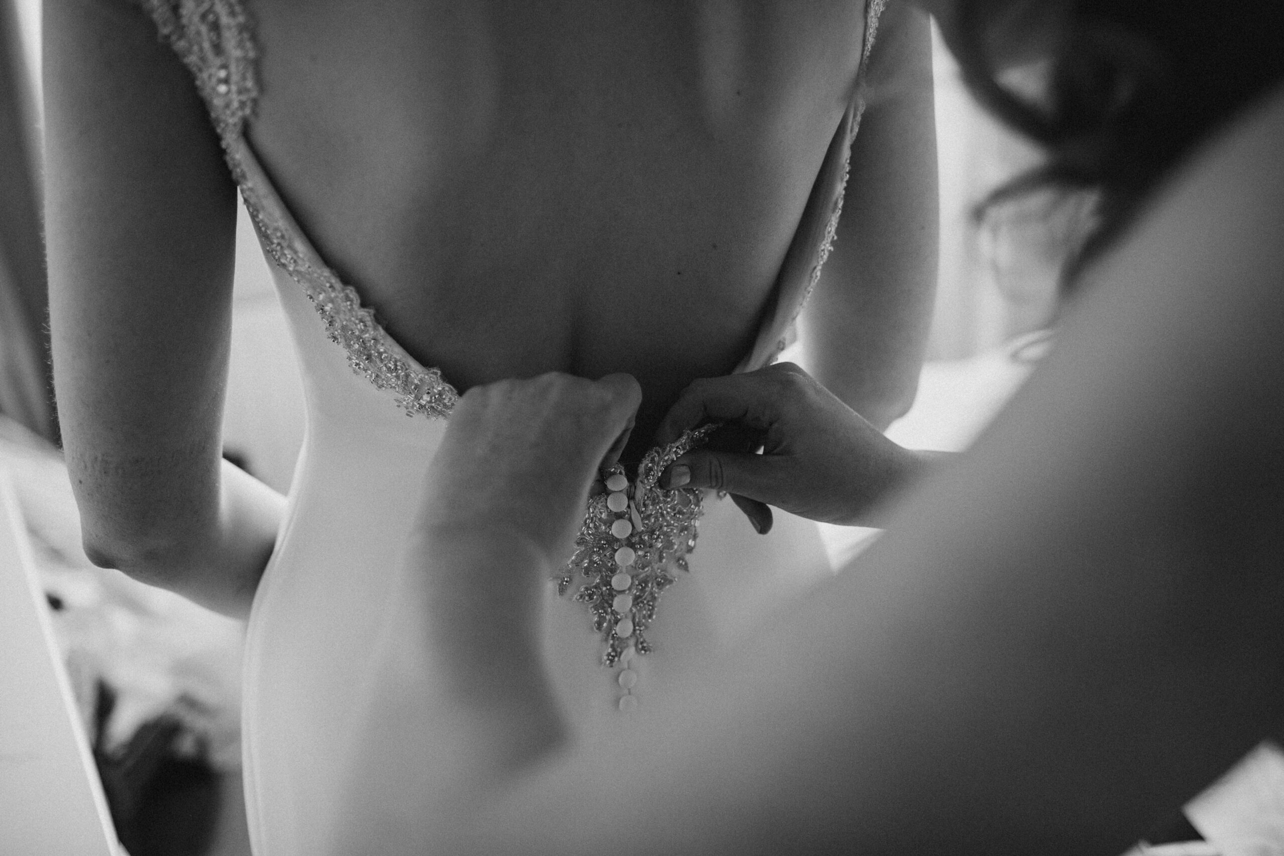black and white photo of bride's dress being done up
