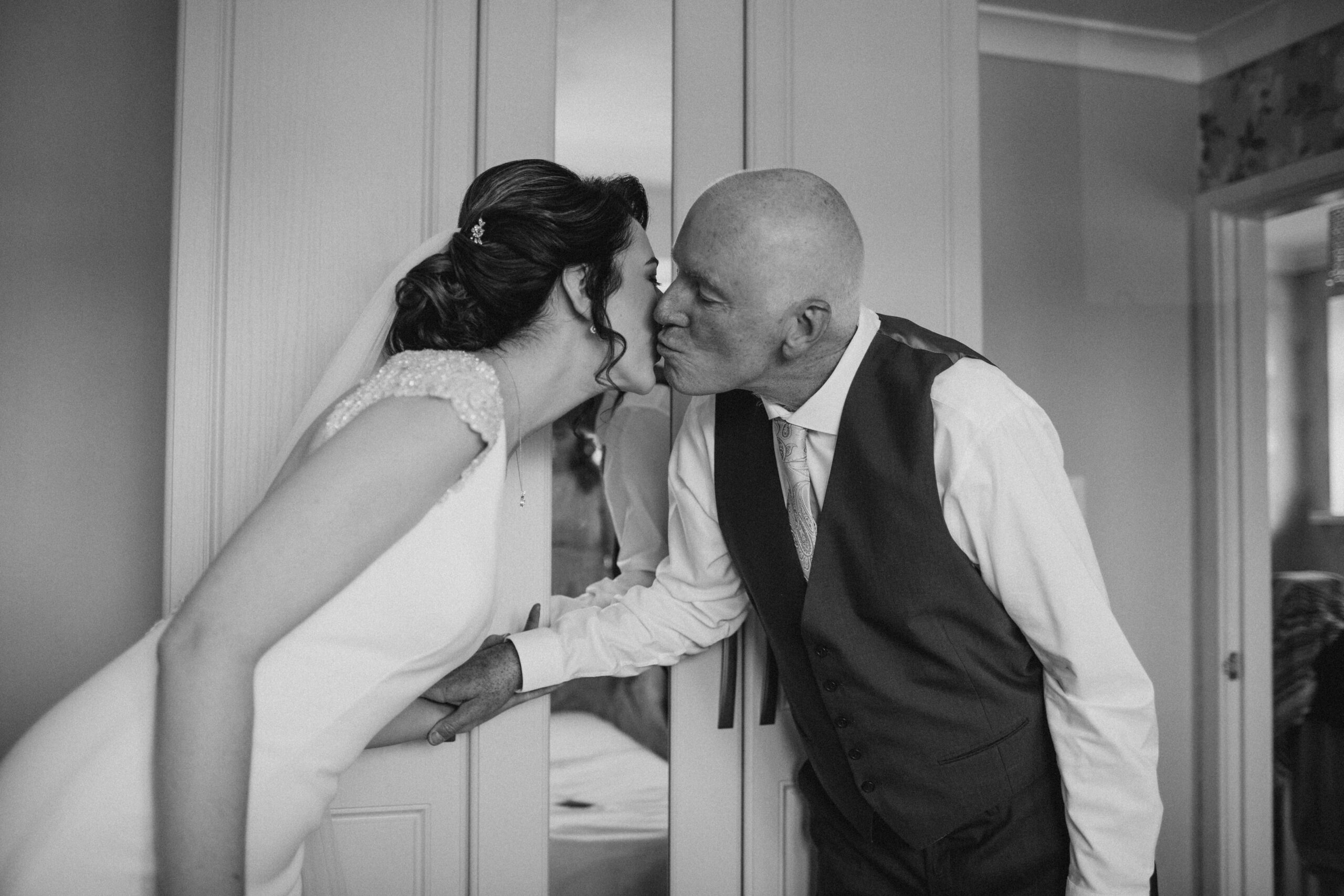 bride's dad seeing bride in dress for first time, kissing her on cheek, black and white image