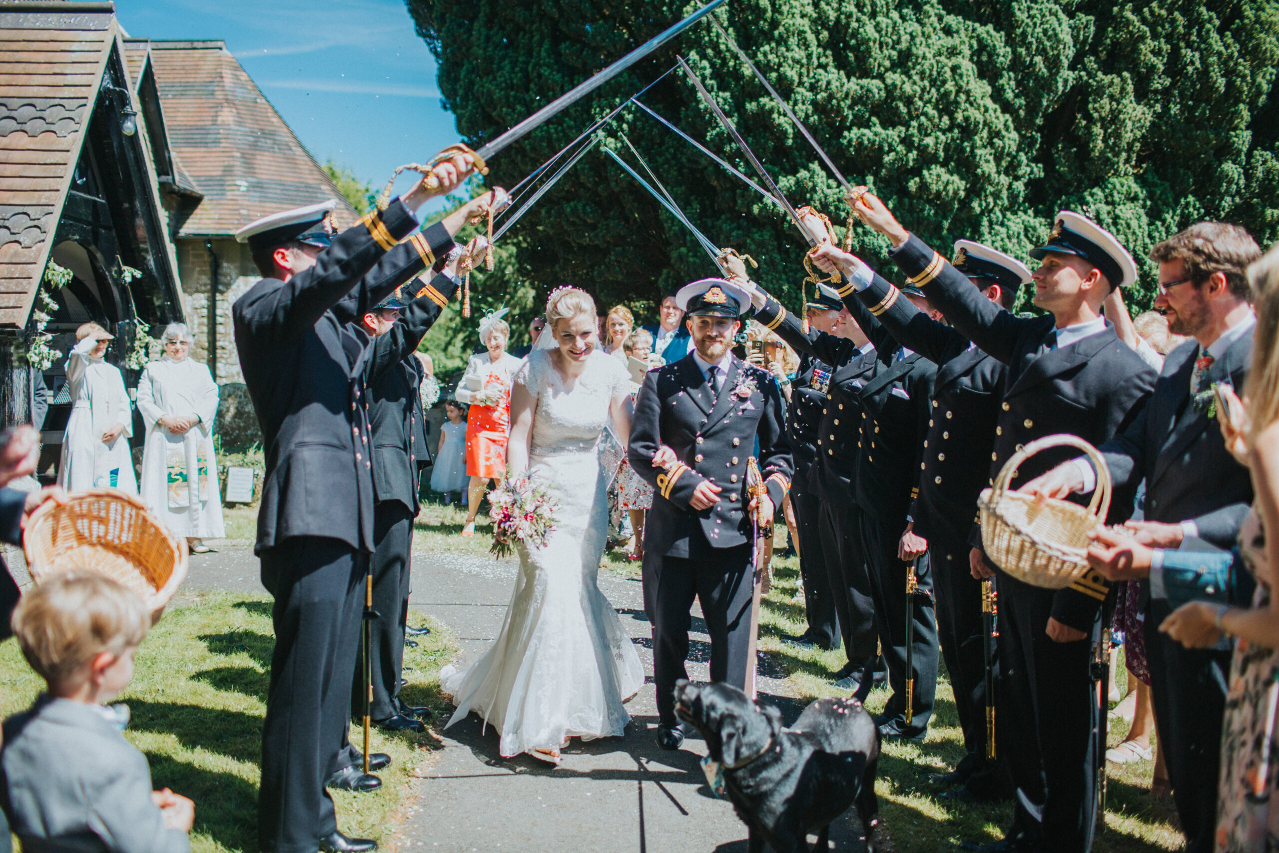 Couple walking through a sword arch with their Labrador, Bella